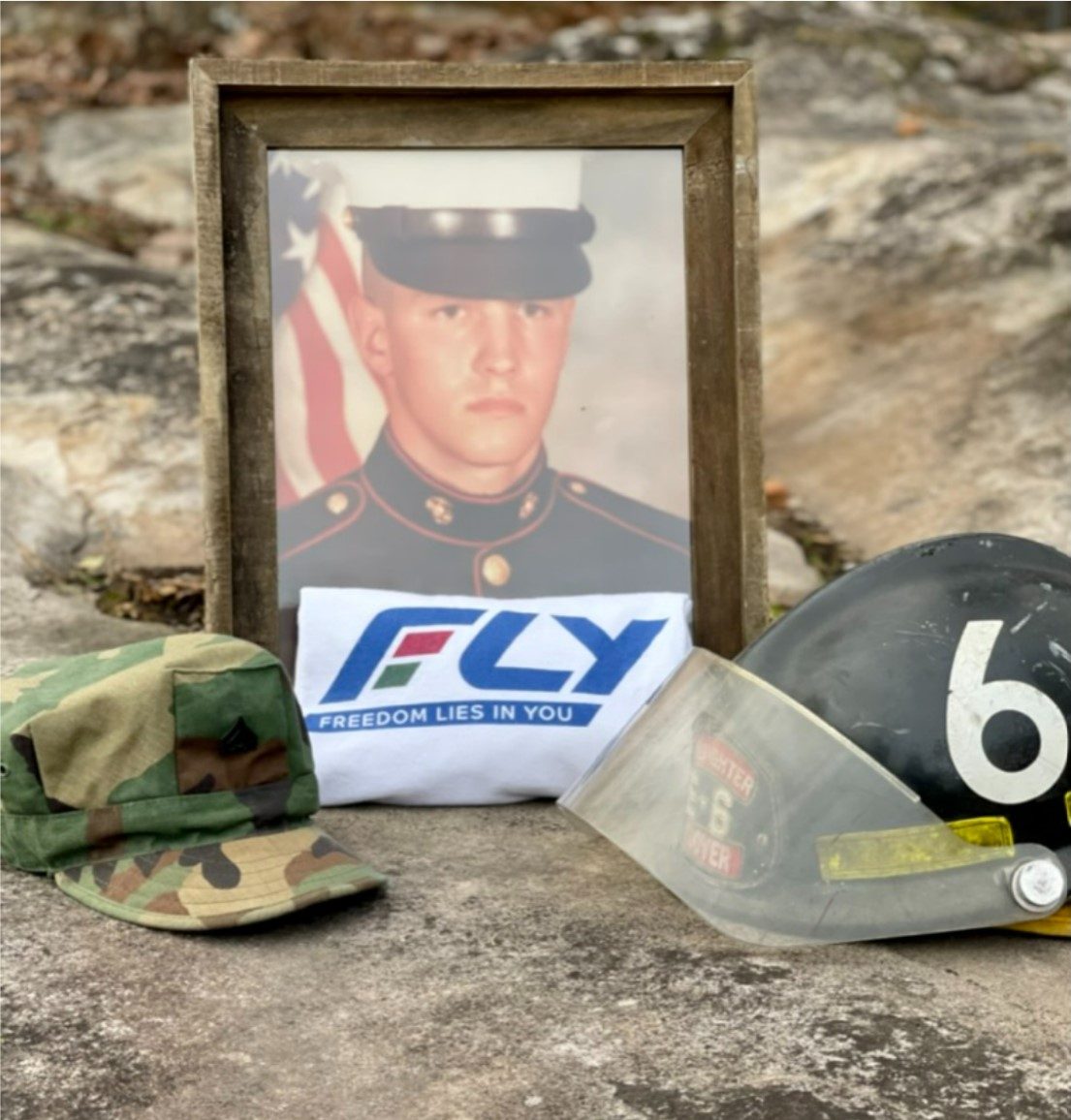 A memorial photo honoring Johnny McKenzie Jr., a Marine Corps veteran and Hoover firefighter, alongside a FLY (Freedom Lies in You) shirt